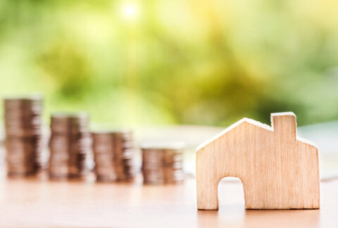 Futuro do mercado imobiliário mostrando uma casa de madeira com moedas atrás