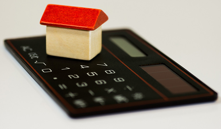Uma casa de brinquedo acima de uma calculadora, demonstrando como o mercado imobiliário é ligado diretamente à economia e pode ser afetado pela estagflação.